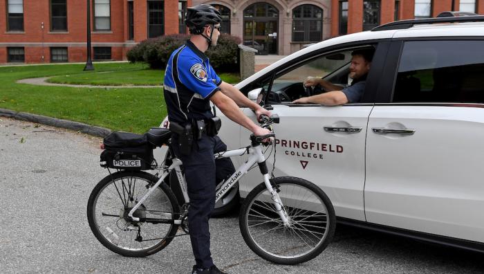 A police officer on a bicycle talks to a College employee in a van