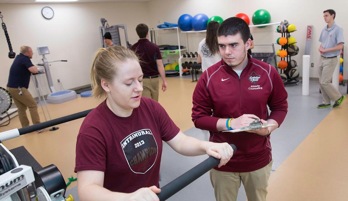 An athletic counseling master's degree student works with a student client in a gym on campus.