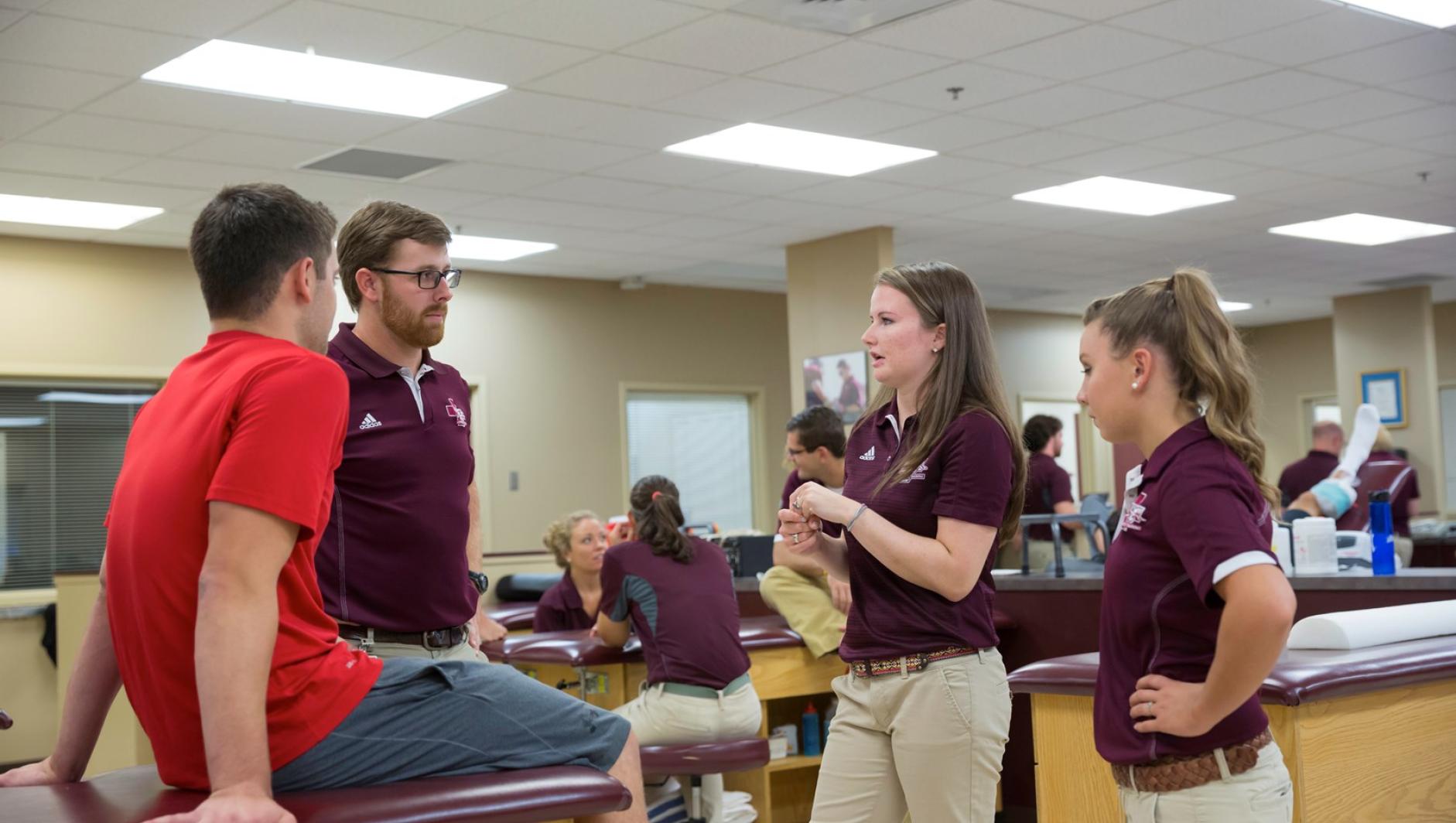 Three athletic training students consult with a client in the athletic training facility