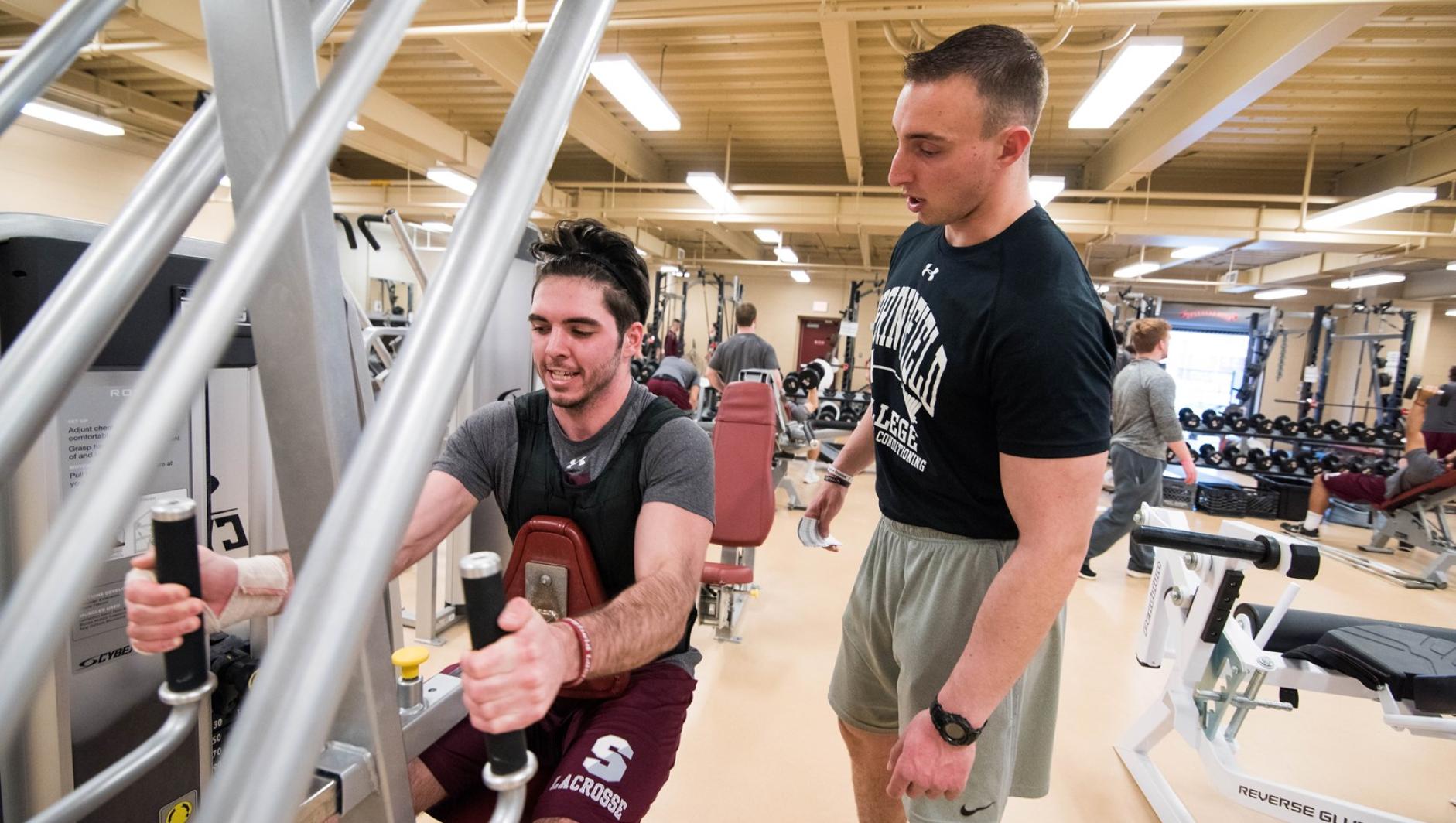 A student strength and conditioning coach looks on as his client used a piece of workout equipment.