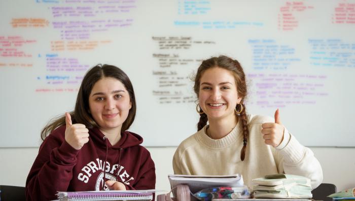 Two students in a classroom, both giving thumbs up